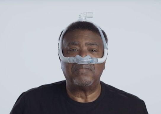 Un hombre usa la mascarilla AirFit N30i de la marca ResMed mientras viste una camisa negra