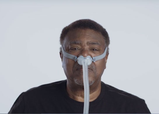 Un hombre con camiseta negra usa la mascarilla AirFit N30i de la marca ResMed