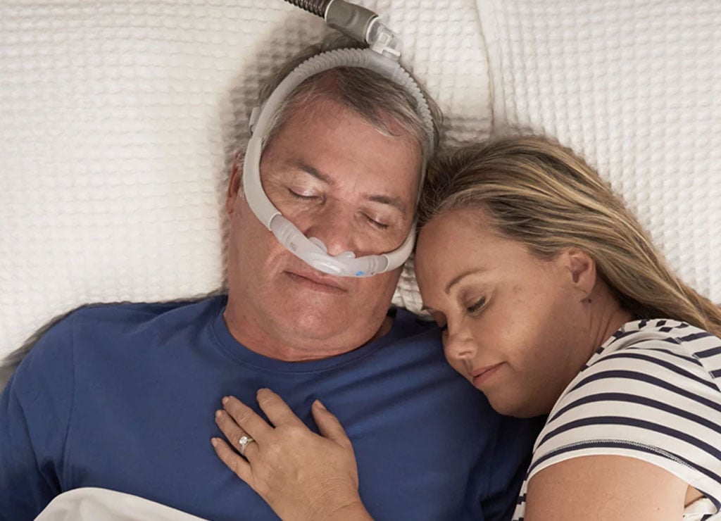 Una pareja duerme mientras el hombre usa la mascarilla AirFit de ResMed