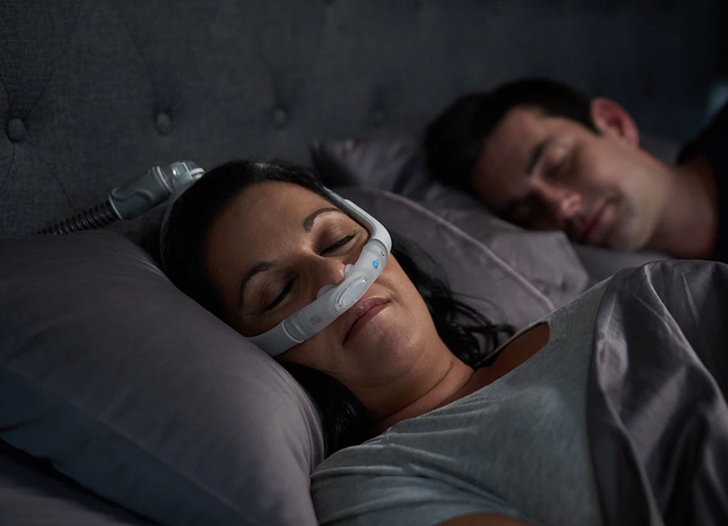Una pareja duerme mientras la mujer usa la mascarilla AirFit de ResMed